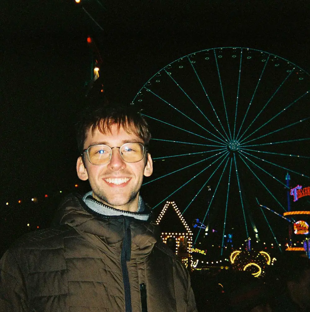Andrius smiling at night in front of a lit Ferris wheel